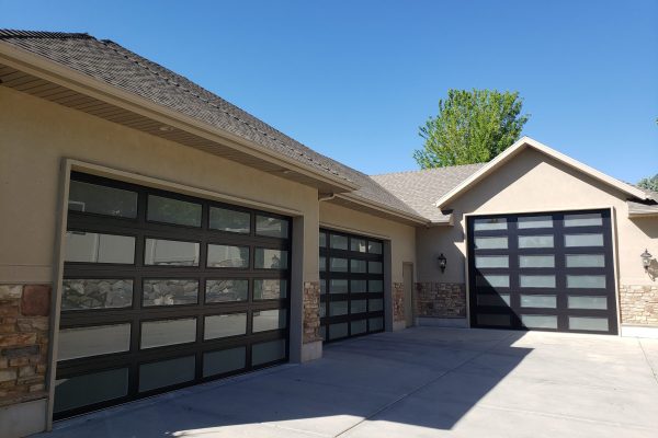 Modern home with three black-framed frosted glass garage doors, set against a beige exterior with stone accents and a concrete driveway under a clear blue sky.