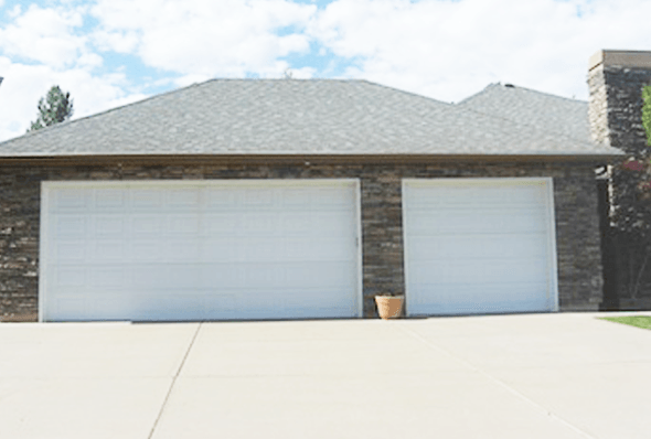 Modern single-story home with stone facade and two large white garage doors, featuring a clean concrete driveway and small decorative planter.